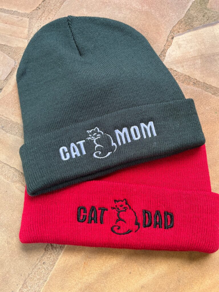 Photo of a green beanie with the words "Cat Mom" in embroidery, and a red beanie with the words "Cat Dad" in embroidery