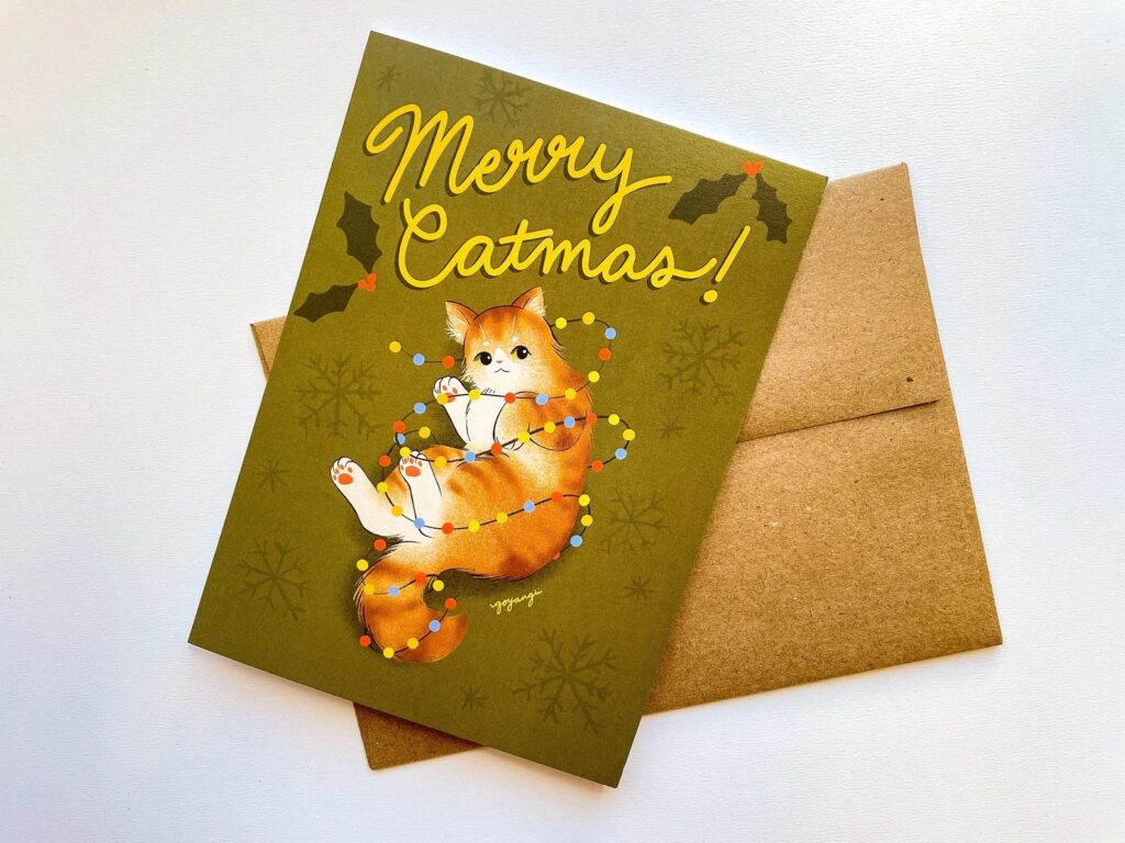 Greeting card with illustration of a cat wrapped up in holiday lights and the caption "Merry Catmas!"
